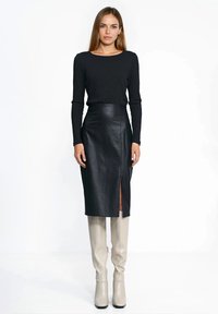 Czarna prążkowana bluzka z długim rękawem zestawiona z czarną, wysoką spódnicą ze skóry z bocznym rozcięciem, do tego beżowe kozaki za kolano.