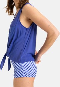 Haut sans manches bleu avec un détail à nouer à la taille, associé à un short rayé bleu et blanc. Tissu doux avec une coupe décontractée.