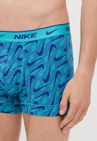 Nike herrboxershorts med ett mönster i blått och turkos med upprepade swoosh-logotyper. Elastisk midjeband med "NIKE"-märkning i blått.