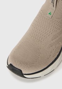 Pantof galesc bej cu un superior din tricot, suprafață texturată și capac de protecție întărit. Dispune de o talpă exterioară din cauciuc negru și un branding minimalist.