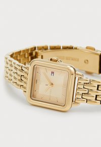 Montre rectangulaire en or avec un cadran décoré et des repères horaires. Dotée d'un bracelet en métal à maillons et d'une fermeture à clip.