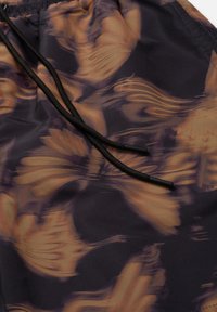 Zwarte trekkoord met plastic uiteinden op patroonshorts met een mengsel van donkerpaars en lichtbruin vloeiende abstracte ontwerpen.