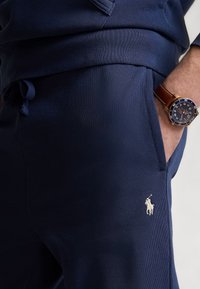 Mörkblå mjukisbyxor i mjukt tyg med elastisk midja och dragsko, sidfickor och en liten vit polologotyp.