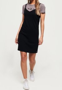 Svart glidkjol med tunna axelremmar över en grå t-shirt, med rund hals och tryckt design. Bärs med vita sneakers.