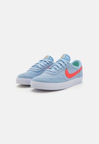 Blaue Wildledersneaker mit weißer Gummisohle, ausgestattet mit einem leuchtend roten Nike-Swoosh und hellblauen Akzenten an der Zunge und dem Futter.