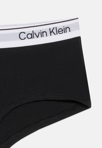 Μαύρο εσώρουχο Calvin Klein με λευκή ζώνη μέσης που φέρει μαύρες και γκρι ρίγες και το όνομα της μάρκας με μαύρο κείμενο.