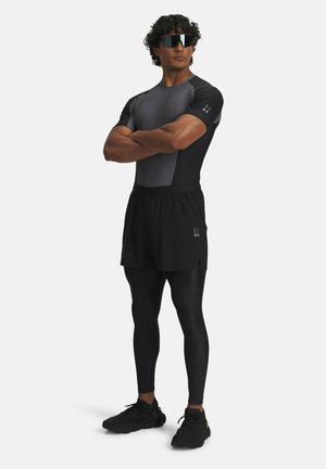 Athletic outfit featuring a fitted black and gray short-sleeve top, black shorts, and black leggings, paired with sporty sunglasses and shoes.