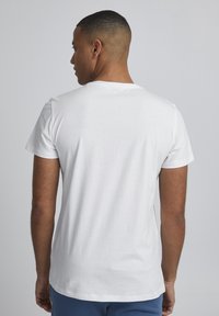 Camiseta de algodón blanca con cuello redondo y mangas cortas, que presenta una textura suave y un corte recto en el dobladillo.