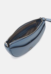 Sac en cuir bleu au design arrondi, fermeture éclair, et deux compartiments intérieurs. Équipé de quincaillerie en ton argent et de détails de logo embossés.