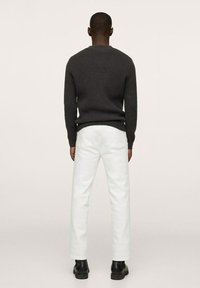 Dunkel gestreifter Pullover, weiße gerade Jeans und schwarze Ankle Boots. Ansicht von hinten mit einem neutralen Hintergrund, der die Texturen der Kleidungsstücke hervorhebt.