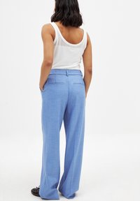 Pantalon large bleu clair en tissu texturé, avec une taille plate, des poches latérales et des détails de poche arrière.