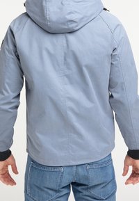 Jasnoniebieska kurtka z kapturem, z gładką teksturą i czarnymi mankietami. Widoczne detale przeszyć i luźny krój.