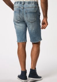 Shorts de mezclilla en azul claro con una cinturilla elástica, dos bolsillos traseros y un dobladillo sin terminar. Combinados con zapatillas altas de color azul oscuro.