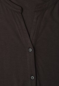 Nærbillede af mørkebrunt stof med V-udskæring og to sorte knapper på et fint ribstrikket beklædningsstykke.