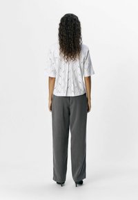 Blouse blanche avec des détails en broderie anglaise et des manches courtes, associée à un pantalon large gris et des talons noirs. Tissu texturé et coupe ample.