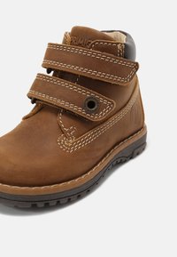 Bottine en cuir marron pour tout-petit avec double bande velcro, coutures blanches et col rembourré noir sur semelle en caoutchouc foncé.