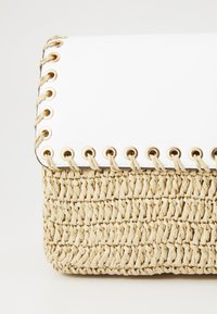 Borsa di paglia intrecciata con una patta sintetica bianca; presenta anelli dorati e cuciture decorative lungo il bordo. Superficie texturizzata, forma rettangolare.