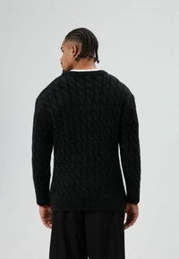 Zwart kabelgebreide trui met een gestructureerd oppervlak, lange mouwen en een ronde halslijn. Voorzien van geribbelde manchetten en zoom.