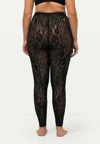 Schwarze Spitzenleggings mit floralen Mustern, einer figurnahe Passform und einem dehnbaren Stoff, der sich dem Körper anpasst.