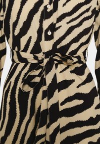 Abito animalier nero e beige con bottoni anteriori, maniche lunghe e cintura annodata in vita per una forma definita. Il tessuto sembra liscio.