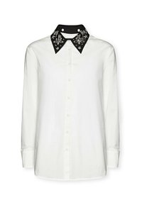 Camicia bianca a maniche lunghe con colletto nero e decorato, caratterizzata da motivi floreali decorativi e chiusura frontale con bottoni.