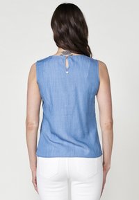 Blusa senza maniche di un leggero blu, realizzata in morbido denim. Caratterizzata da un collo rotondo, dettaglio a chiave sul retro e orlo leggermente svasato.