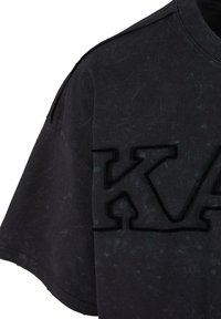 Melna pārmērīgi liela t-krekla ar teksturētu "KA" logotipu priekšpusē. Materiāls izskatās nedaudz nolietots ar maigu, matētu apdari.