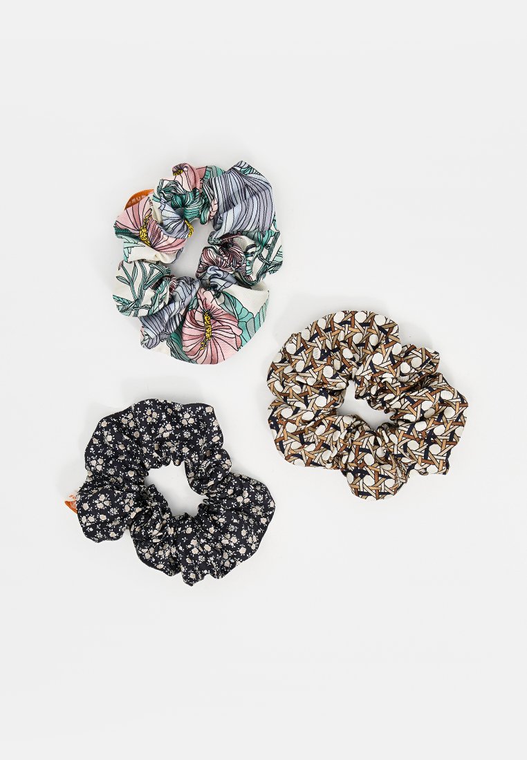 Three fabric hair scrunchies are displayed: one with a floral and leafy pattern, one in black with small flowers, and one with an abstract design.