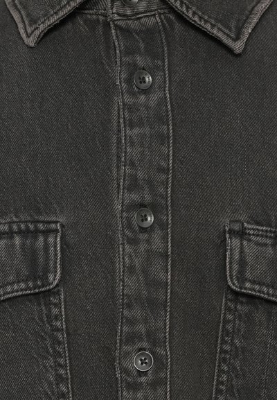 Schwarze Jeanshemd mit spitzem Kragen, sechs Knöpfen auf der Vorderseite und zwei Brusttaschen mit geraden Kanten. Die Textur ist leicht grob.