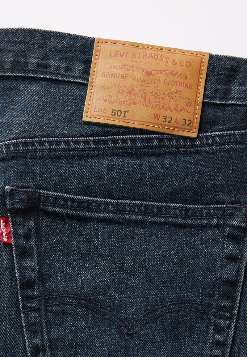 Donkerdenim jeans met een leren label. Label met reliëftekst, Lot 501, en W 32 L 32. Rode tag op de zak met stikseldetails.