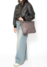 Borsa a tracolla trapuntata grigia con catena, caratterizzata da una forma rettangolare e materiale in pelle morbida. Il modello indossa una giacca bomber nera e jeans azzurri.