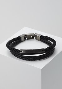 Bracelet noir tressé avec des brins de cuir et de cordon entrelacés, fermoir métallique, texture lisse et subtile brillance sur les accents en métal.