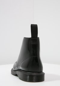 Botín Chelsea negro de goma con un acabado liso y brillante, panel lateral elástico y suela texturizada con un tacón bajo y tira de agarre.