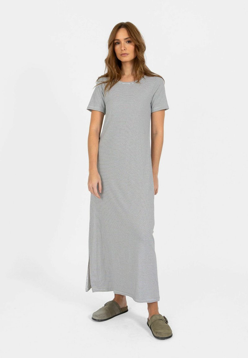 Femme debout portant une robe à manches courtes, longue jusqu'aux chevilles, rayée gris et blanc avec des fentes latérales, et des chaussures slip-on vert olive.