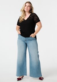 Zwarte V-hals top met kanten mouwen, gecombineerd met lichtblauwe wijde jeans. Het ensemble heeft een ontspannen pasvorm en casual stijl.