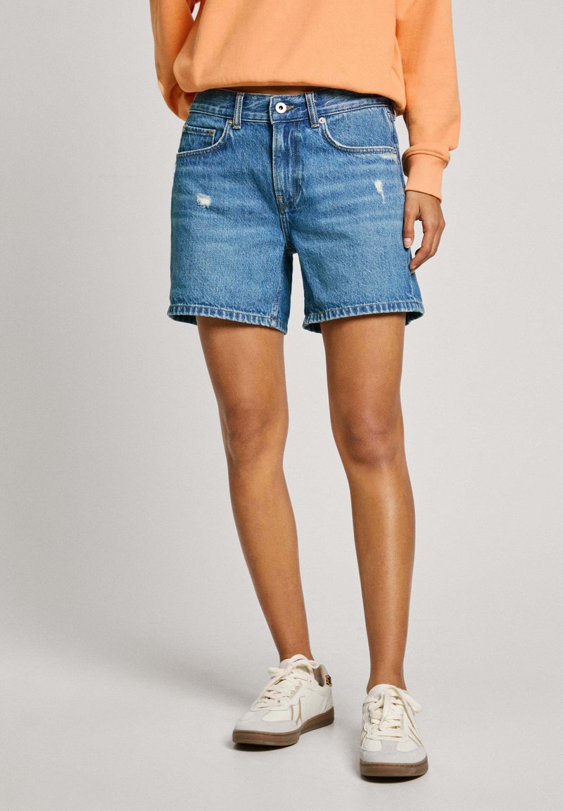 Shorts en denim bleu clair avec un design usé, un ourlet effiloché et un style classique à cinq poches. Associés à des baskets blanches.