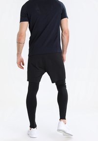 Schwarze Sportshorts über schwarzen Leggings getragen, kombiniert mit einem marineblauen kurzärmligen Shirt mit strukturiertem Design auf der Rückseite.