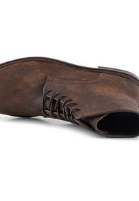 Botas de tobillo de ante marrón con cordones, punta redondeada, superficie texturizada y costura visible a lo largo de la suela.