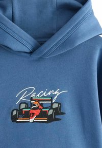 Haut en coton bleu avec un design de voiture de course coloré brodé et le mot "Racing" en écriture blanche au-dessus.