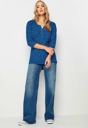 Blå leopardmønster bluse med tre fjerdedele ærmer, parret med brede lyseblå jeans og hvide sneakers. Enkel halsudskæring.