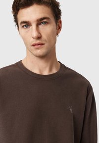 Felpa marrone a coste con scollo rotondo e dettaglio logo discreto. Presenta un tessuto strutturato e una vestibilità ampia per il massimo comfort.