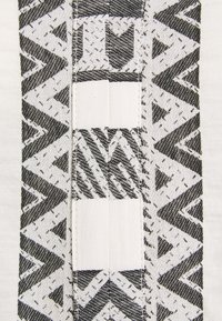 Textil en blanco y negro con patrones geométricos en zigzag y secciones texturizadas. La tela tiene una superficie lisa con diseños contrastantes.