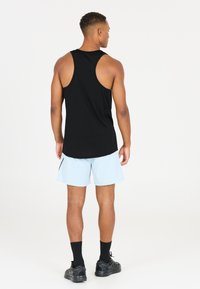 Svart ärmlös idrottstopp, ljusblå shorts och svarta träningsskor. Slt glatt tyg, avslappnad passform och kontrasterande sömdetalj.
