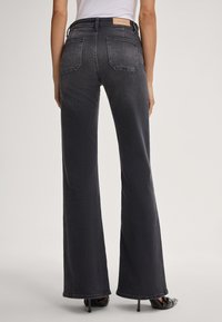 Hoge taille, uitlopende spijkerbroek van donkergrijze denim. Bevat twee achterzakken en een merketiket aan de taille. Zachte textuur, onafgewerkte zoom.