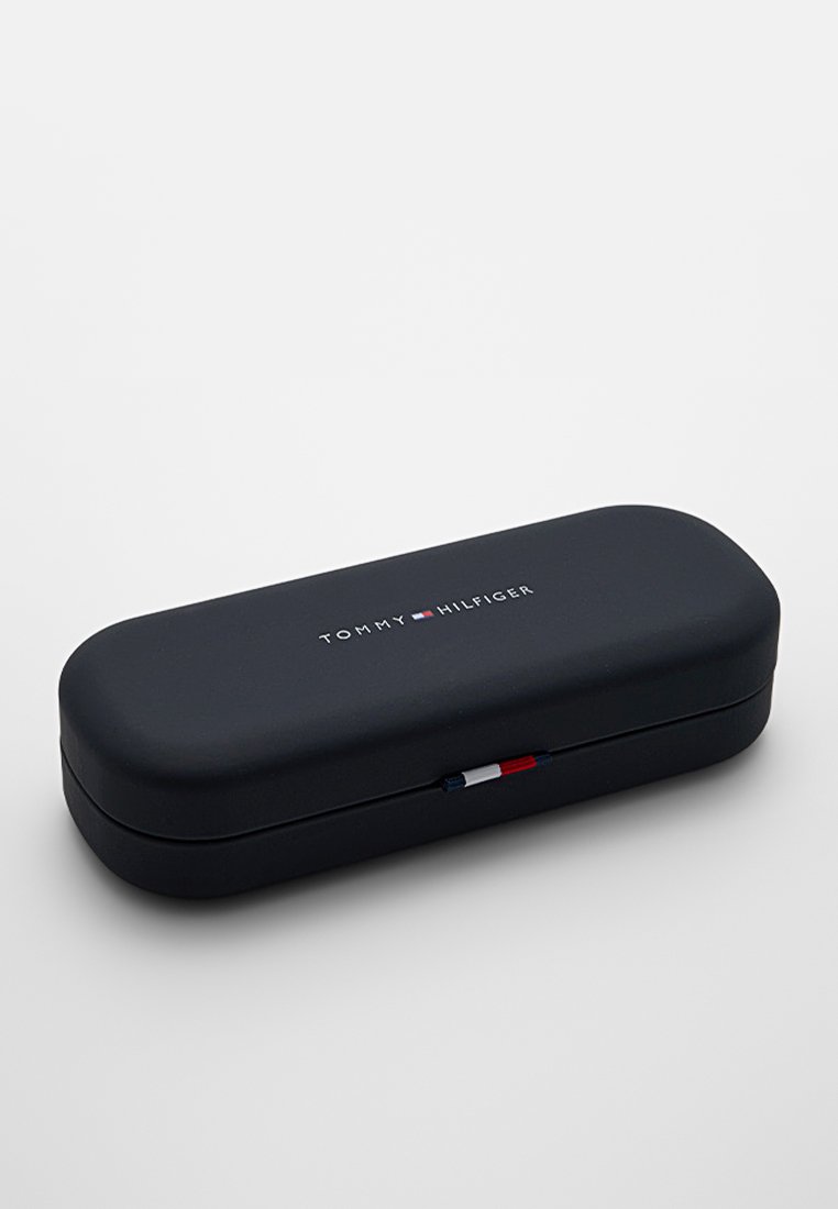 Custodia per occhiali Tommy Hilfiger, forma ovale, esterno nero opaco, logo in testo bianco, piccolo design rosso, bianco e blu sul gancio.