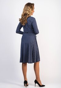 Marindräkt med lång ärm och en flödande kjol med ett vitt abstrakt mönster. Inkluderar ett knyt i midjan och komplementeras av svarta klackar.