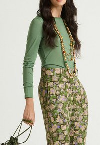 Maglia verde a maniche lunghe abbinata a pantaloni verdi con motivo floreale e tocchi di viola e beige. Accessoriata con una collana a più fili di perline.