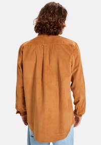 Bruine corduroy overhemd met lange mouwen, knoopmanchetten en een achterplooitje, met een afgeronde zoom en een gladde textuur.