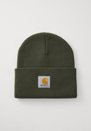 Berretto lavorato a maglia verde con risvolto. Presenta un'etichetta quadrata bianca con un logo giallo e il nome del marchio "Carhartt" in lettere nere.