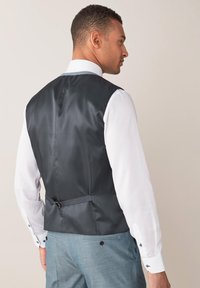 Tamno sivi satenasti prsluk elegantnog dizajna, s podesivim remenom straga, nosi se preko svijetle košulje.